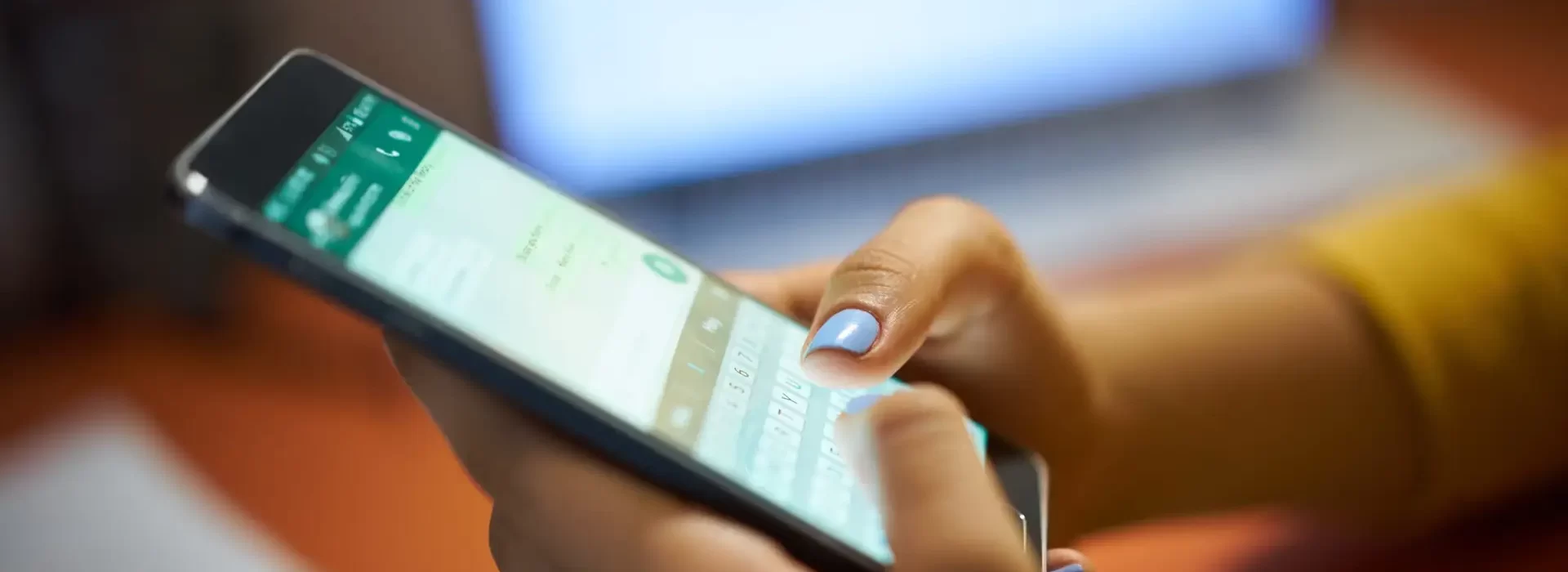 Girl Typing Phone Message On Social Network At Night Young woman using cell phone to send text message on social network at night. Closeup of hands with computer laptop in background